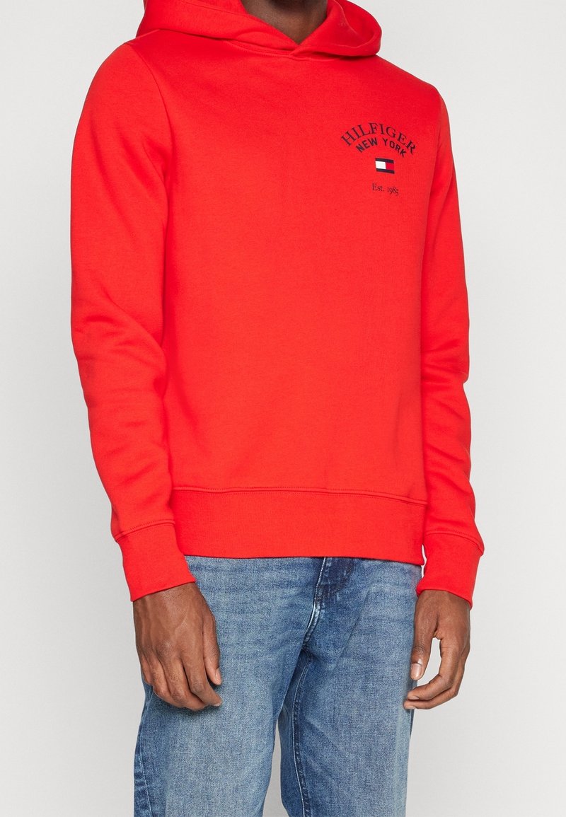 Rode hoodie van zacht materiaal, met een kangoeroezak, ribbelmanchetten en een ribbelband, voorzien van een logotextontwerp aan de voorkant.