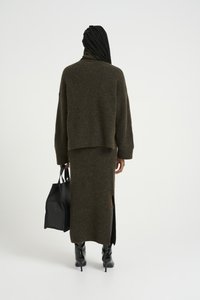 Suéter marrón de punto con cuello alto combinado con una falda larga a juego que presenta una abertura lateral, complementado con un bolso tote negro y botas altas hasta la rodilla.