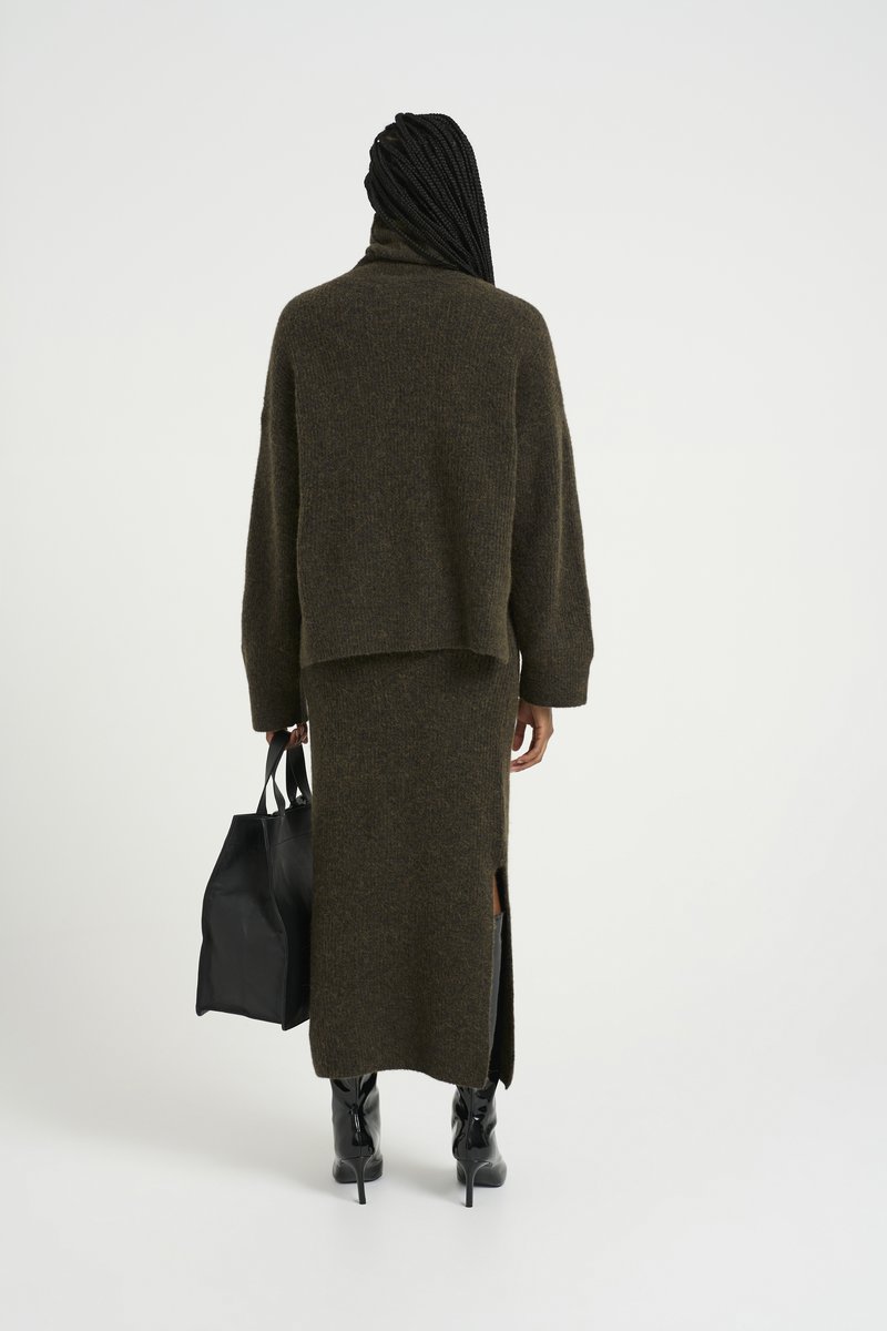 Maglione brown lavorato a maglia con collo alto abbinato a una lunga gonna coordinata con uno spacco laterale, completato da una borsa a tracolla nera e stivali al ginocchio.