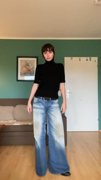 Black short-sleeve turtleneck top paired with wide-leg faded blue jeans featuring light distressing and a dark leather belt.