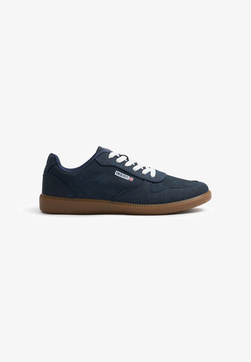 Zapatillas de lona navy con cordones blancos, suela de goma y textura sutil; presenta una etiqueta de logo en el lado y un diseño redondeado.