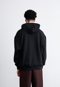 Sort oversized hoodie med snøre i hætten, blødt stof og ribbede manchetter, parret med teksturerede mørkebrune bukser med et subtilt mønster.