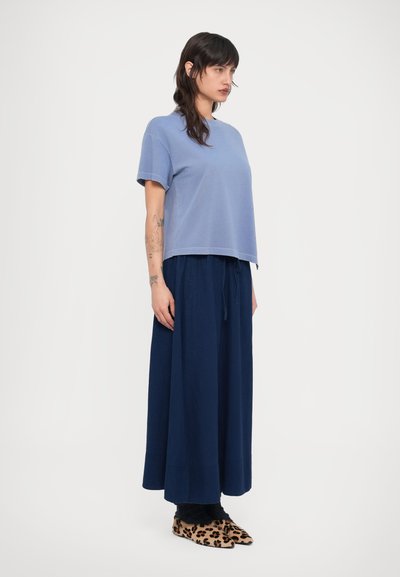 Ανοιχτό γαλάζιο κοντομάνικο τοπ, χαλαρή σκούρα μπλε μακριά φούστα και παπούτσια με εκτύπωση λεοπάρδαλης. Το ύφασμα φαίνεται απαλό, με ομοιόμορφη υφή και άνετη εφαρμογή.