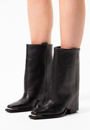 Bottines en cuir noir avec un design replié, bouts pointus et semelles plates. Présente un look minimaliste et une texture lisse.