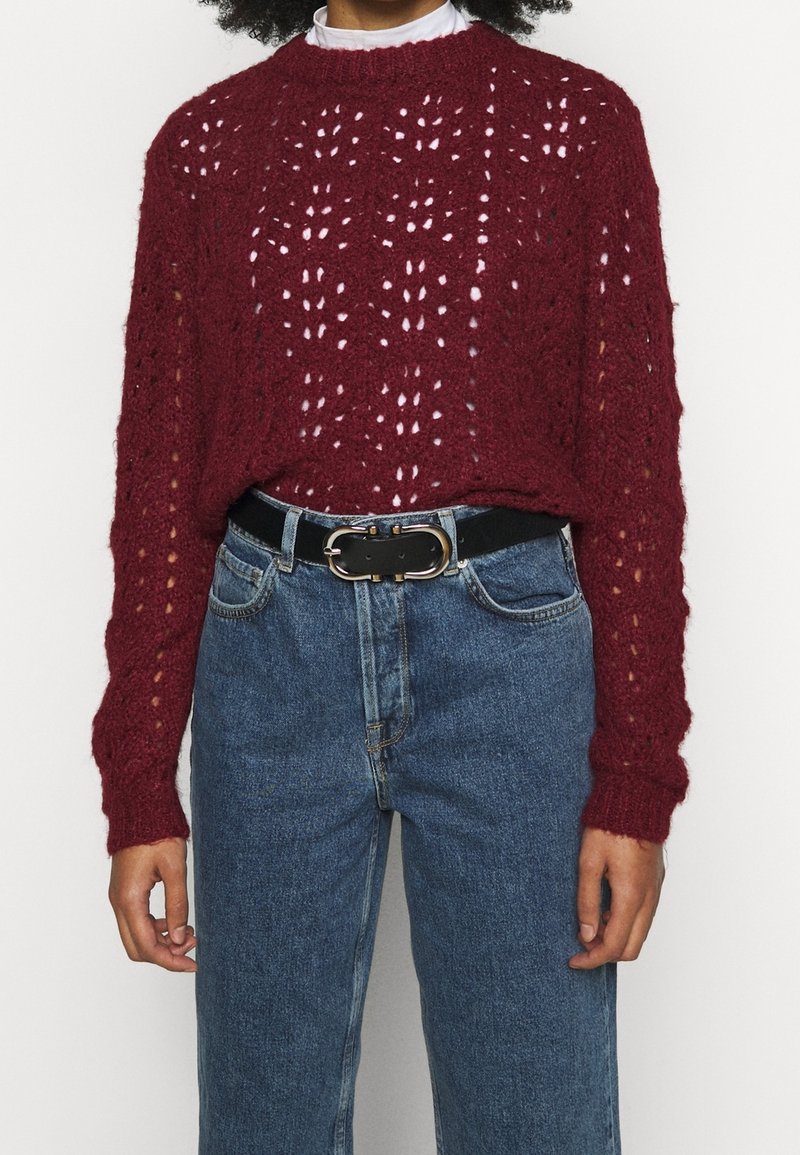 Maglione bordeaux a maglia con motivi a punto aperto, colletto rotondo e maniche lunghe, abbinato a jeans blu a vita alta e una cintura nera.