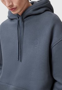 Felpa grigia con cappuccio dal texture morbida, cordini regolabili e logo ricamato. Dispone di una tasca a marsupio e polsini a coste.
