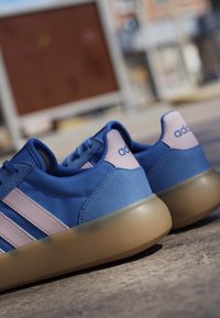 Blue Adidas sneakers with pink stripes and heel detail, featuring a thick translucent brown sole, positioned on a concrete surface.