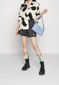Camicia a maniche corte con motivo bianco e nero, pantaloni corti neri con logo, calze a pois colorate fino al ginocchio, stivali neri con lacci e borsa blu.