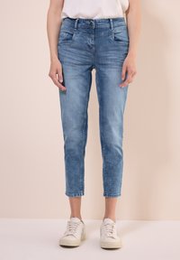 Ljust blå denimjeans med slim fit, med knappstängning, framfickor och uppvikta anklar. Bärs med vita sneakers.