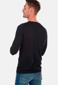 Schwarz langärmliges Shirt aus leichtem Material, mit Rundhalsausschnitt und subtiler Textur, kombiniert mit blauen Denim-Jeans.