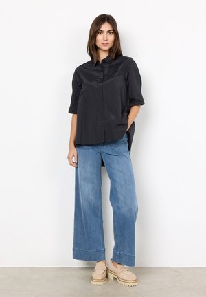 Black button-up shirt with short sleeves, paired with wide-leg light blue jeans and beige platform loafers, set against a plain background.