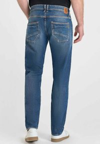 Jeans in denim blu con taglio dritto, dotati di una fascia in pelle in vita, tasche posteriori con cuciture e leggeri segni di usura sul tessuto.