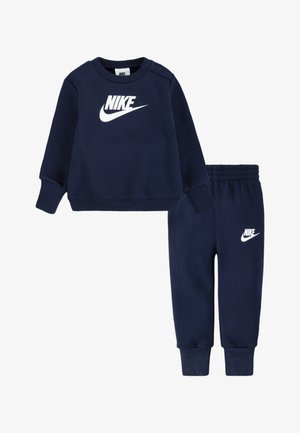 Tamsiai mėlynas džemperio ir kelnių komplektas, pagamintas iš minkšto medvilnės mišinio. Priekyje yra baltas „Nike“ logotipas ir elastingas liemens diržas, užtikrinantis patogumą.