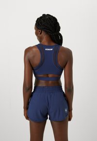 Sujetador deportivo azul marino con detalles de malla y logo en la parte posterior; combinado con pantalones cortos azules marinos a juego con una cinturilla elástica y bolsillos laterales.