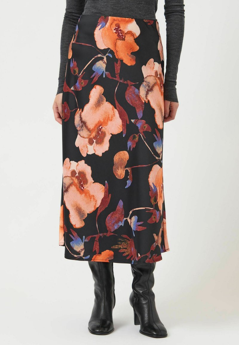 Falda maxi floral en tela negra con flores vibrantes en naranja y azul, con una abertura en el dobladillo y textura suave, combinada con botas negras hasta la rodilla.