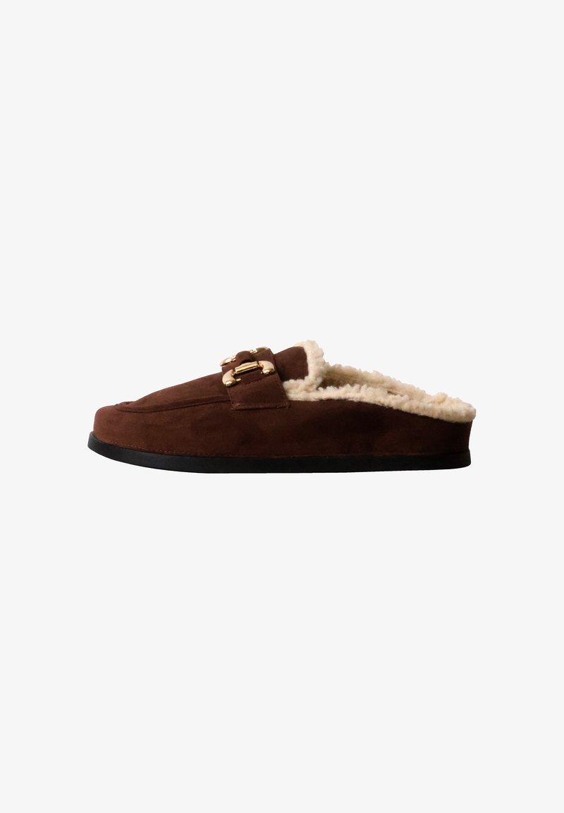 Chausson en suède marron à enfiler avec doublure en polaire couleur crème et boucle dorée décorative sur semelle noire, vu de côté.