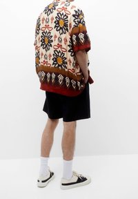 Chemise à manches courtes avec un motif floral en beige, rouge et noir. Assortie à un short noir et des baskets avec des accents crème.