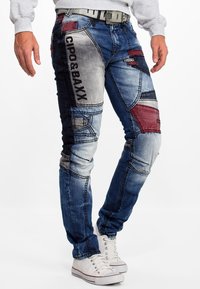 Denim jeans met een patchworkdesign in tinten blauw, rode accenten, geborduurd merk op de zijkant en een slim fit.