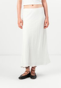 White maxi skirt, lightweight fabric, slightly flared design, smooth texture, worn with black lace-up flats. Solid color, no patterns.
