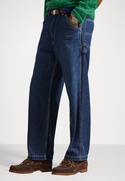 Tumed sinised denim püksid mugava lõikega, küljetaskudega ja nähtava õmblusega. Kombineeritud pruuni nahkse pidevuga.