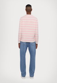 Črtasta jopica v svetlo roza in sivi barvi, pletena tekstura. V kombinaciji z svetlo modrimi širokimi džins hlačami in belimi supergami. Pogledu zadaj.