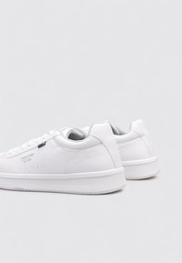 Zapatillas blancas con parte superior de cuero texturizado, suela de goma y detalles con costuras. Presentan un logo lateral y diseño con cordones.