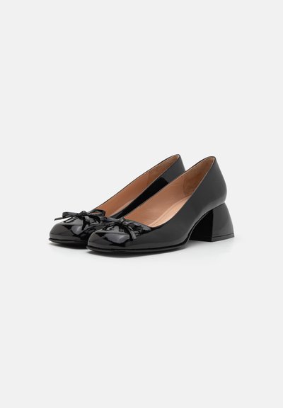 Schwarze Lacklederschuhe mit runder Zehenform, verziert mit einer Schleife und einem klobigen Absatz. Glatte Textur mit glänzendem Finish.