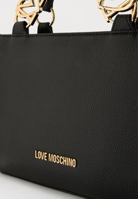 Μαύρη τσάντα χειρός από δέρμα με υφή και χρυσά μεταλλικά στοιχεία, με εμφανές λογότυπο "LOVE MOSCHINO" και καλλιτεχνικές χειρολαβές στην κορυφή.