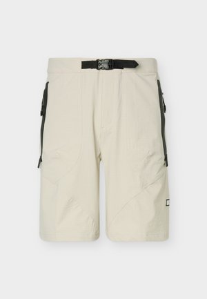 Svetlo bež kratke hlače dolžine do kolen z črnimi stranskimi žepki z zadrgo in nastavljivim črnim pasom z zaponko na enobarvnem ozadju.