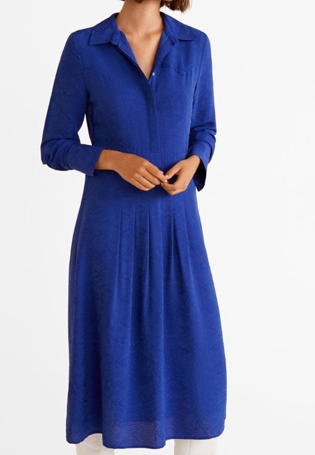 Femme portant une robe midi bleu roi à manches longues avec col et des plis à partir de la taille, mains légèrement croisées devant.