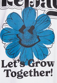 Weißes T-Shirt mit einem blauen Blumenmotiv, das ein lächelndes Gesicht zeigt, schwarzen Konturen und dem Text "Lass uns gemeinsam wachsen!" in fetter schwarzer Schrift.