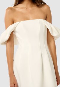 Vestido blanco sin mangas con corsé estructurado, mangas curvadas y costuras verticales. Tela suave con una silueta ajustada y dobladillo acampanado.