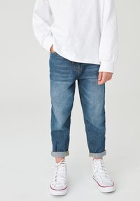 Jeans di denim blu con una vestibilità rilassata, orli risvoltati e una leggera sbiaditura. Abbinati a sneakers bianche con un accento rosso.