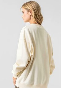 Sudadera de crema, de corte holgado, con cuello redondo, hombros caídos, mangas largas, textura suave, con detalles mínimos, sin patrones visibles.