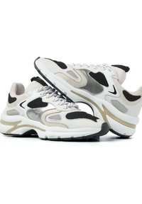 Baskets blanches et beiges avec des accents en maille noire, présentant un design épuré, des matériaux texturés et une semelle arrondie avec une bande dorée.