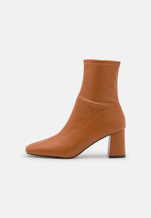 Botte en cuir marron montant à la cheville avec un bout pointu et un talon bloc, vue de profil sur fond blanc.