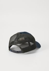 Donkere mesh trucker pet met verstelbare snapback en een solide blauwe gebogen rand, getoond van achteren op een lichte achtergrond.