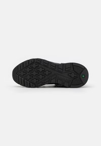 Czarna gumowa podeszwa buta posiada teksturowany wzór z przyczepnymi wypustkami oraz zielonym akcentem. Oznaczona logo "Timberland".