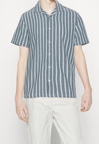 Pruhovaná košile s krátkým rukávem v barvě tyrkysové a bílé, s límcem, knoflíkovým zapínáním, strukturovanou tkaninou a vertikálními pruhy.