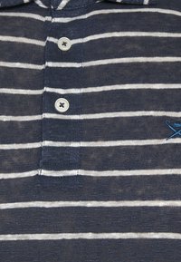 Camisa polo azul marino con rayas horizontales blancas, con un cuello de tres botones y detalles bordados. Tejido suave con un acabado texturizado.