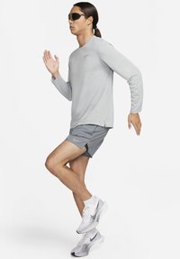 Vaaleanharmaa pitkähihainen urheilupaita ja siihen sopivat shortsit, joissa on tummia yksityiskohtia. Päällä tummat aurinkolasit ja valkoiset, harmaat sekä mustat juoksukengät.