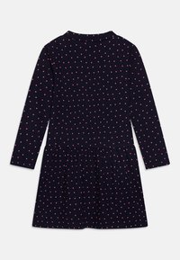 Dlouhé šaty z tmavé látky s růžovými puntíky, s nařaseným pasem a rozšířenou sukní.