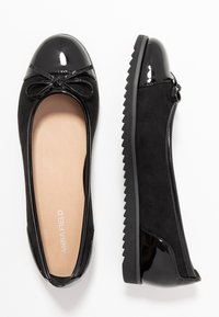 Bailarinas negras con puntera de charol brillante, cuerpo de ante, detalle de lazo y suela de goma texturizada.