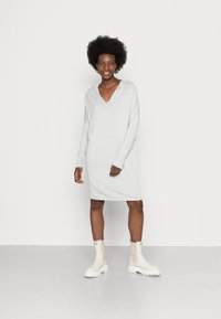 Vestido tricotado cinza claro com decote em V, mangas longas e detalhes canelados. Combinado com botas brancas até ao tornozelo com solas grossas.