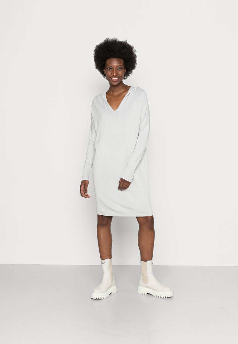 Vestido tricotado cinza claro com decote em V, mangas longas e detalhes canelados. Combinado com botas brancas até ao tornozelo com solas grossas.