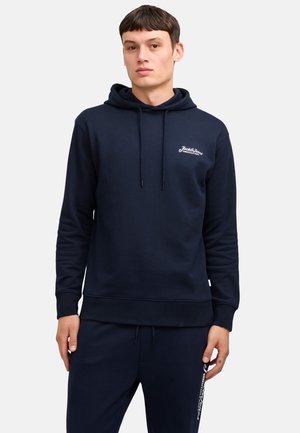 Felpa con cappuccio blu navy realizzata in morbido tessuto, con logo anteriore in bianco, cordini e polsini a costine. Indossata con pantaloni abbinati.