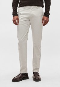 Beezhikarva nuhkse lõikega püksid, millel on sile tekstuur ja esimesed taskud. Sobitatud tumepruunide loafersidega, et saavutada viimistletud välimus.