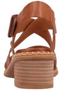 Brown leather sandal with crossed straps and an ankle buckle. Features a textured stacked heel and decorative stitching along the sole.