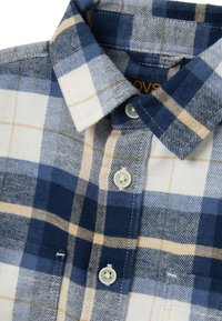 Camicia a quadri blu e bianca con accenti gialli. Presenta un colletto a punta, due tasche frontali e bottoni in plastica.