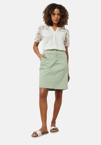 Blusa blanca con bordados de recortes florales, con botones en la parte delantera; falda de algodón verde con dos bolsillos; sandalias blancas con hebilla y suela de corcho.